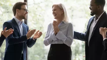 Group of colleagues clapping and celebrating together indoors.
